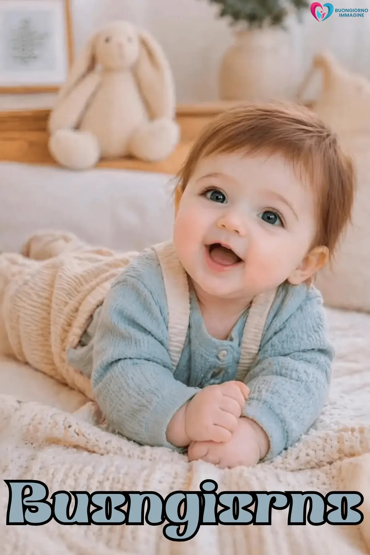 Neonato sorridente in cardigan azzurro su copertina beige, buongiorno bambini immagini gratis per WhatsApp