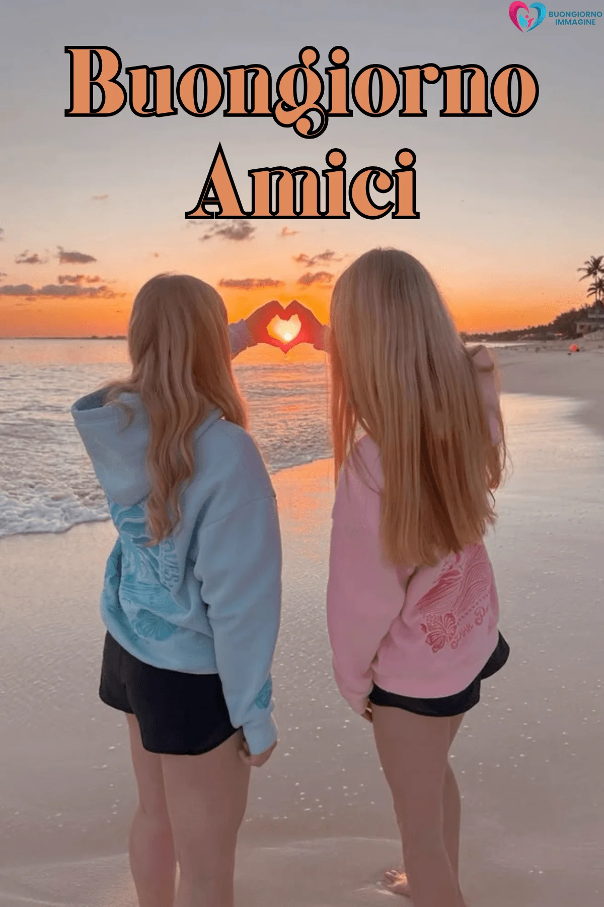 Due amiche al tramonto in spiaggia formano un cuore con le mani – buongiorno amici immagini gratis per WhatsApp